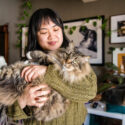 Woman cradling a long haired cat in her home.