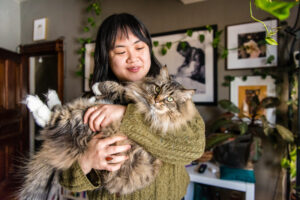 Woman cradling a long haired cat in her home.